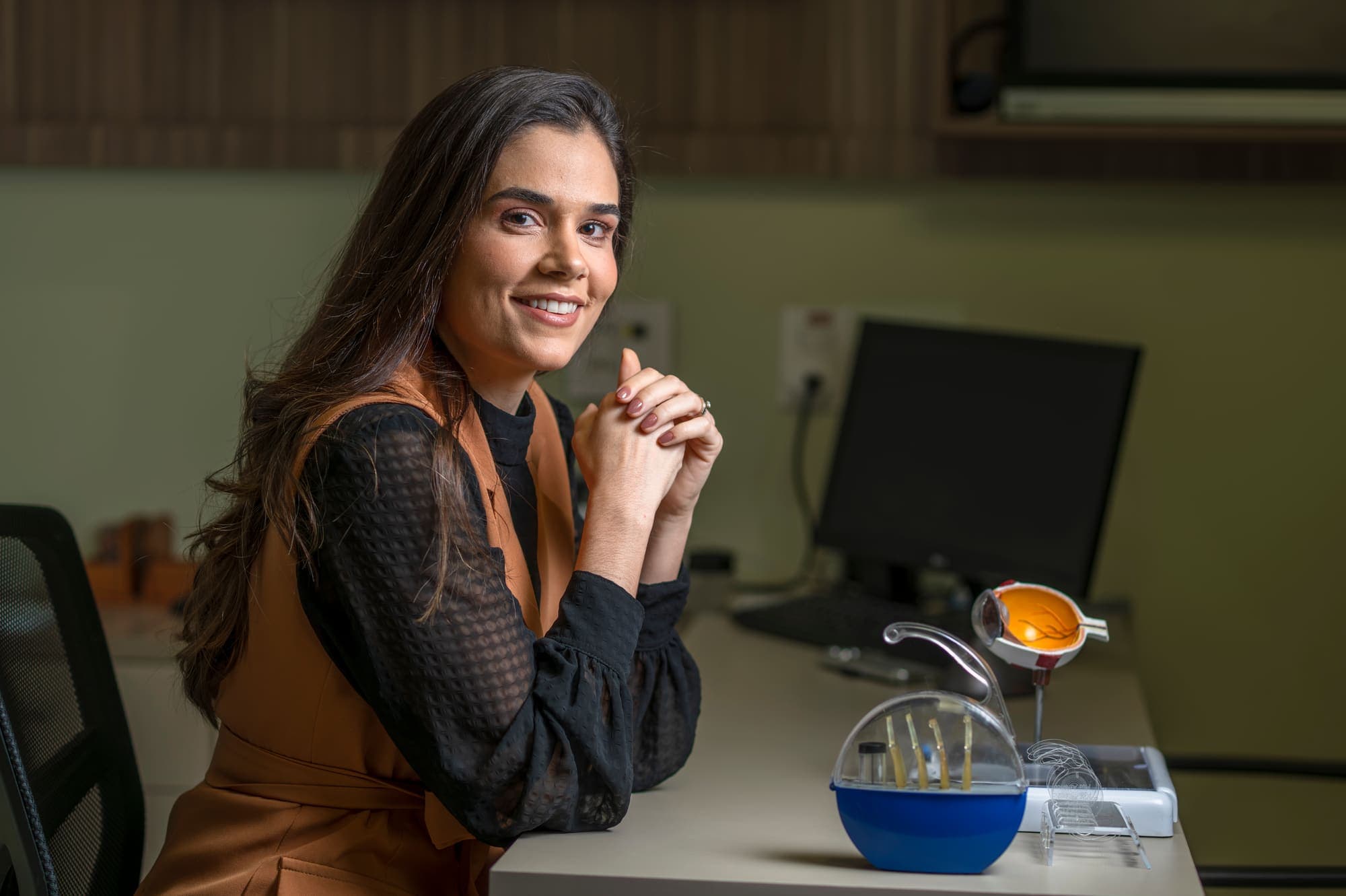 Dra. Mariana Lopes sorrindo à mesa, com modelos anatômicos do olho